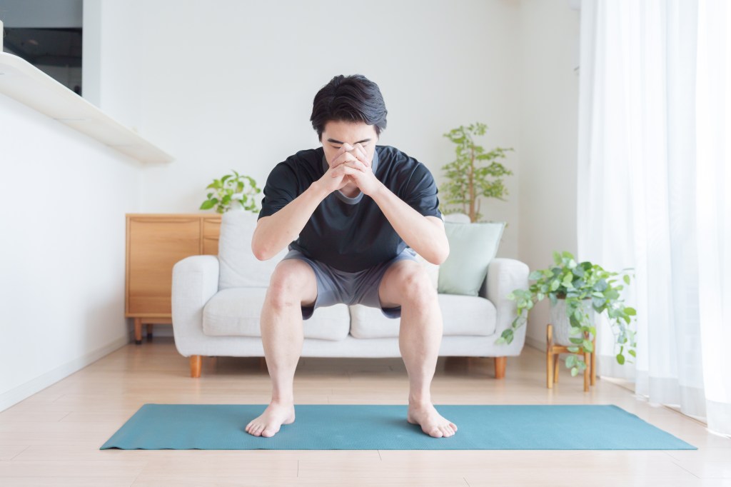 Man doing squats barefoot in living room.