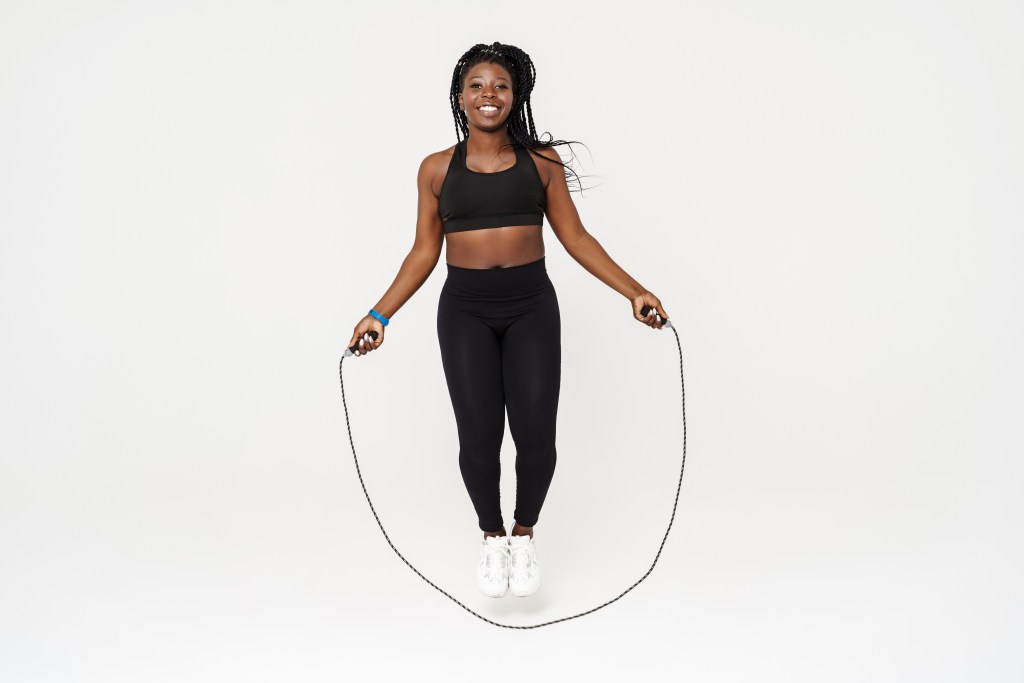 Black young sportswoman working out with a jumping rope on a white background