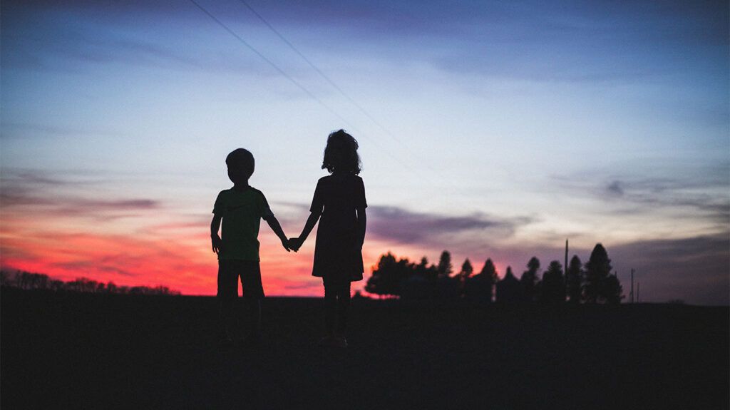 silhouettes of two children against the sky at twilight