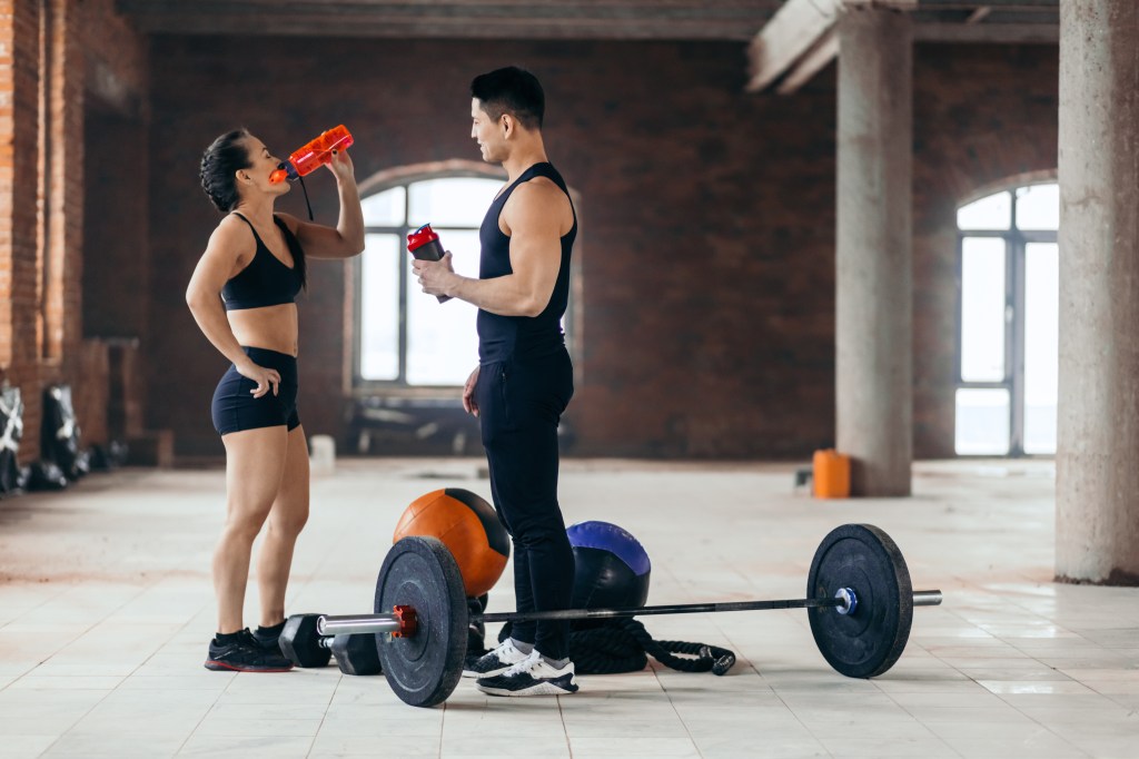 Young man and woman in gym attire drinking water during a fitness training session