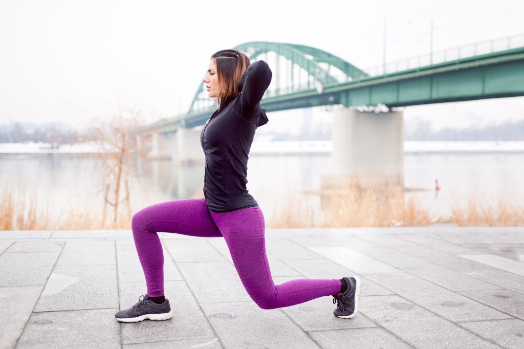 A fitness woman performing a split squat exercise outdoors