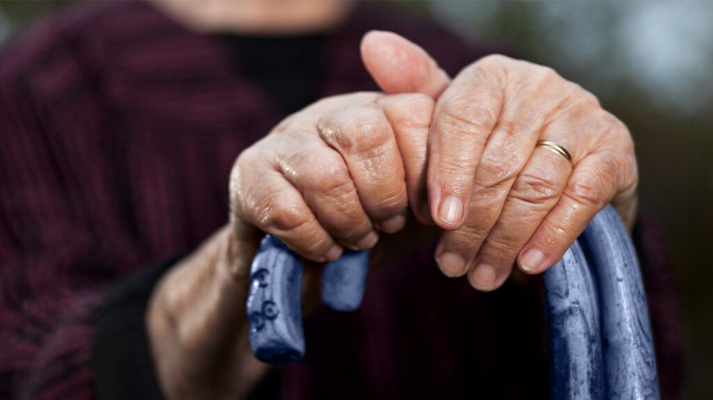 An older adult holding on to a walking stick for support in getting up