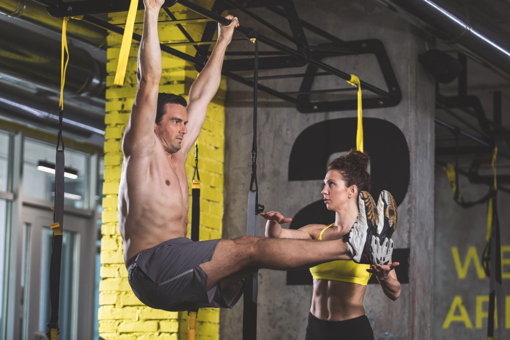 Man in a side view doing abdominal crunches with the assistance of a focused female trainer