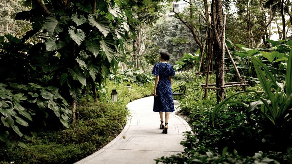 person in blue dress with white dots walking down an alley in a lush green park