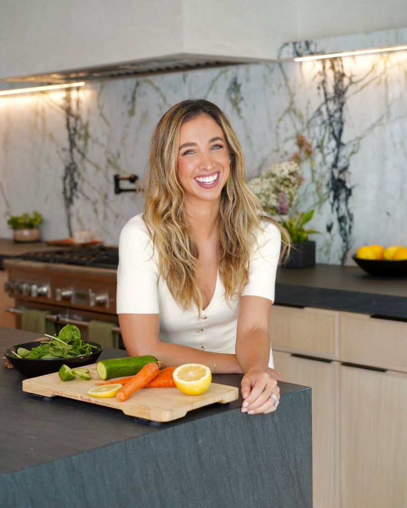 Katie Austin smiling for the camera with a chopping board of vegetables in a kitchen.