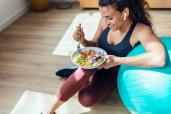 You don't have to spend a lot of money on the latest programs to get the best weight loss results. Here, a woman eats a healthy bowl of food while resting her arm on an exercise ball.