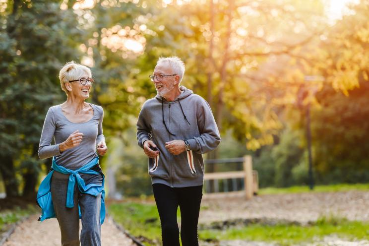 Senior couple with smiles on their faces jogging together in a park.