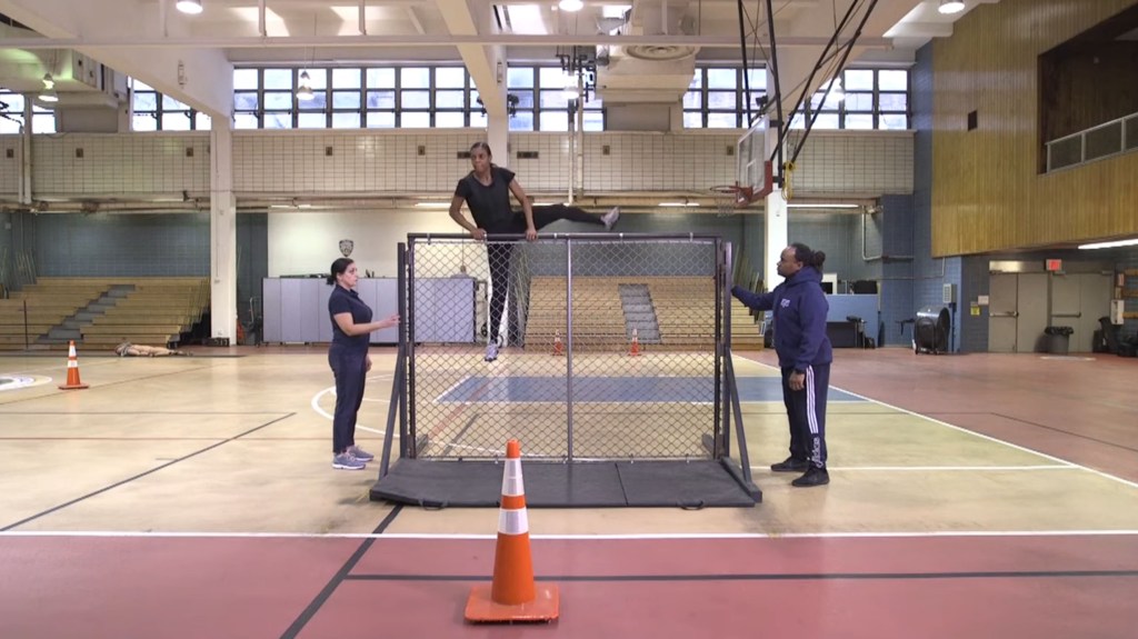 Police academy recruit climbing a fence as part of the NYPD's physical fitness test.