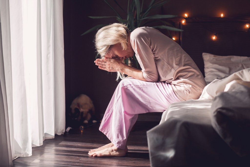 Middle-aged woman looking distressed while sitting on bed at home, touching her hair
