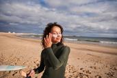 Woman in wetsuit applying sunscreen at the beach.